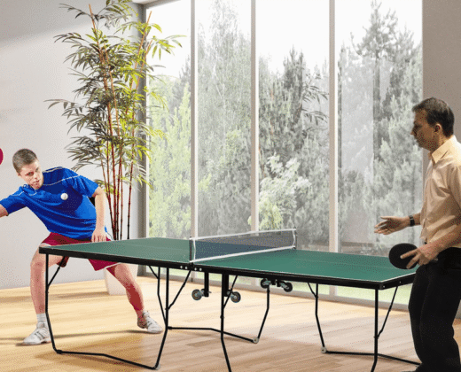 two men playing ping pong on a green table tennis table with a white net, standing on a wooden floor with large glass windows in the background