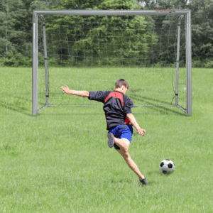 A boy in a black shirt and blue shorts about to kick a football into an empty goal