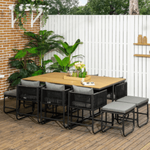a 11 piece black rattan dining set with a table and 10 chairs, outside on a wood decking with white fencing and plants behind