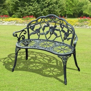 a green cast aluminium decorative garden bench on a garden lawn with flower borders in the background