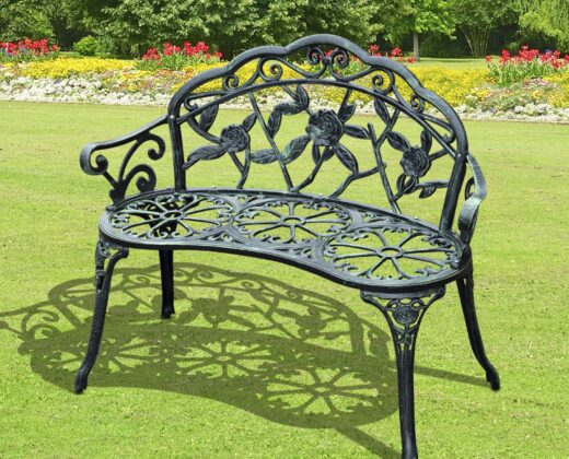 a green cast aluminium decorative garden bench on a garden lawn with flower borders in the background