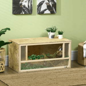 a wooden reptile terrarium with a glass front and air hole panels, containing a green lizard climbing onto a small branch with green leaves