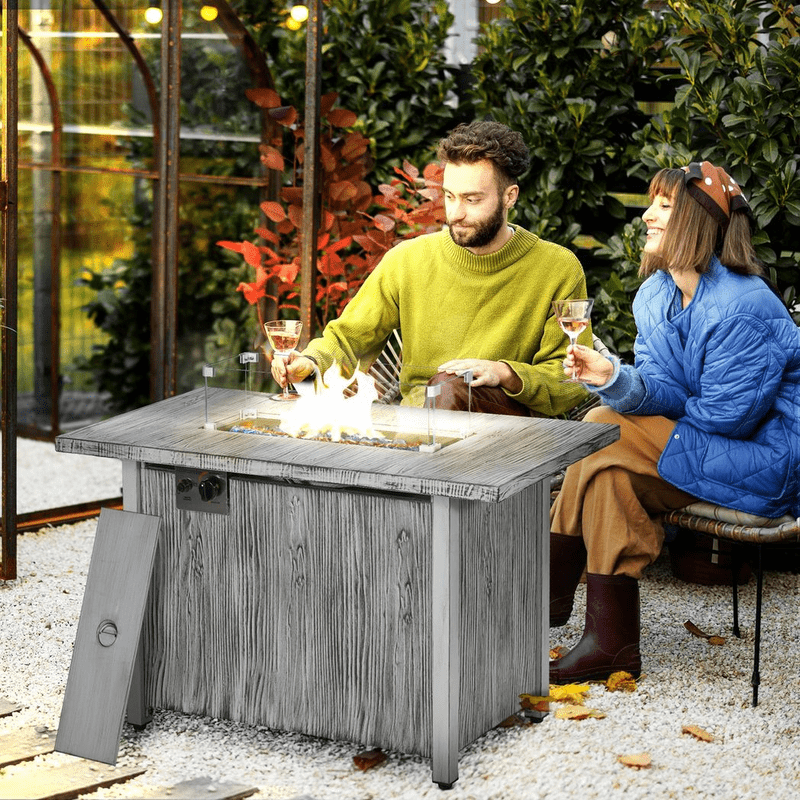 a man and a woman sitting in the garden drinking wine, keeping warm by a grey gas fire pit table