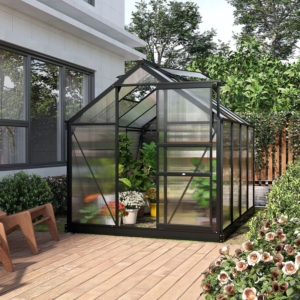 a black 6ft x 8ft walk-in greenhouse in a garden with wood decking, flowers and bushes